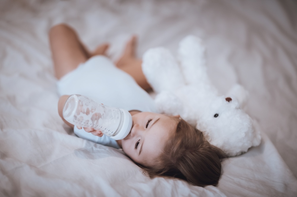 Sweet Adorable Child Lying Down in His Bed with His Best Friend, Soft Toy Teddy Bear and Eating Formula. Preparing To Nap. Healthy Babies Life.. Happy Healthy Childhood