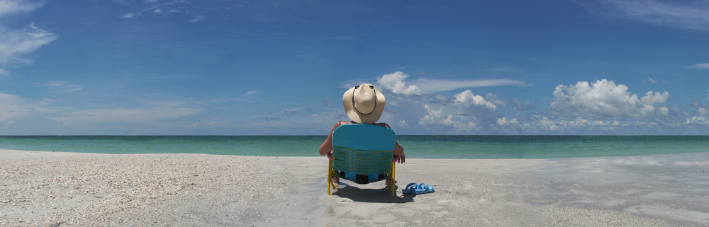 Woman wering sun hat seating in chair sunbathing by waters edge