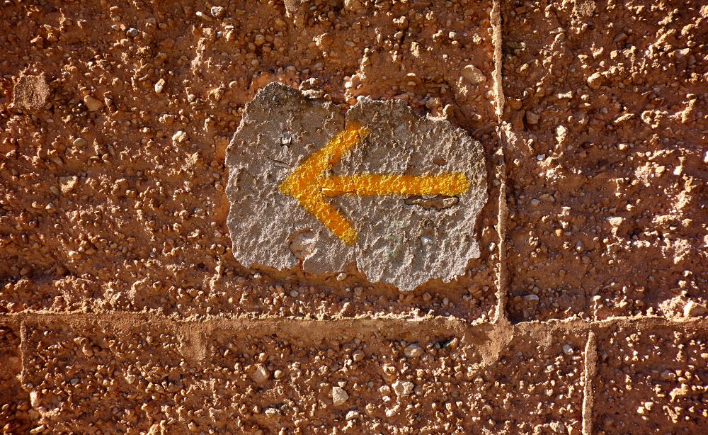 Yellow arrow sign of Camino de Santiago way of Saint James pilgrims in adobe wall