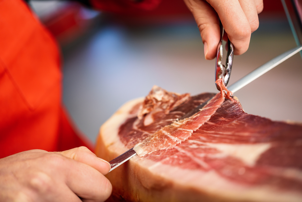 Close-up of professional cutter carving slices from a whole bone-in serrano ham