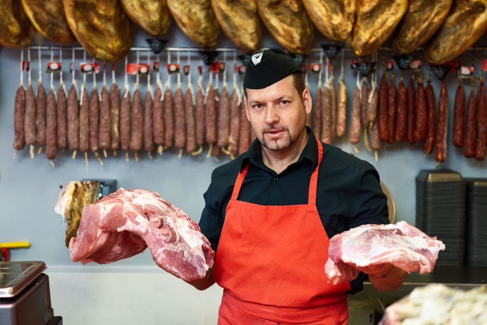 Portrait of a handsome butcher holding meat standing in a butcher shop