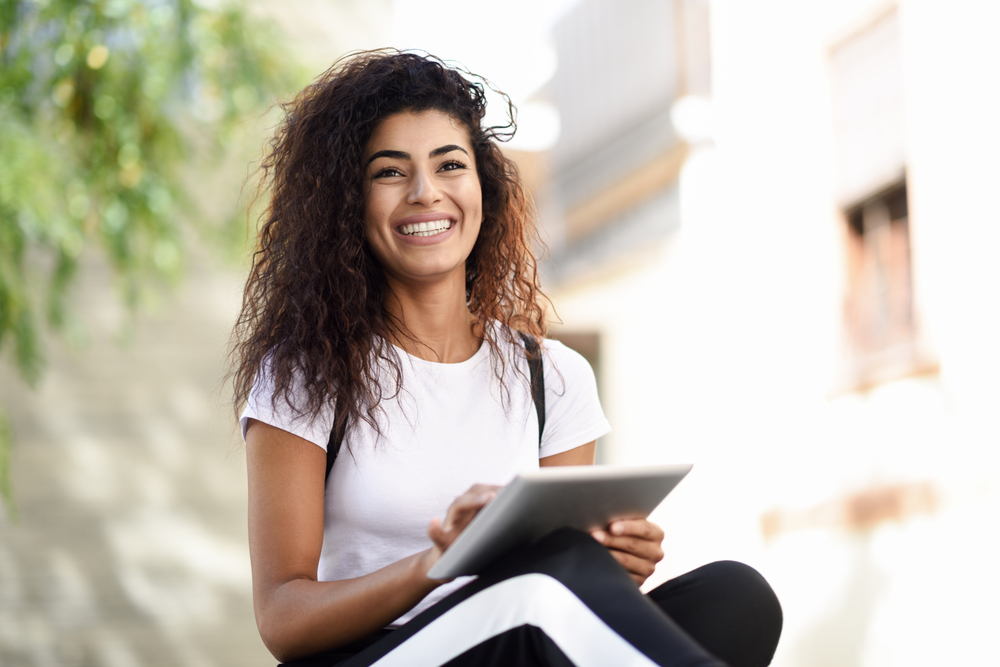 Smiling African woman using digital tablet outdoors. Happy Arab girl wearing sportswear and smiling in urban background