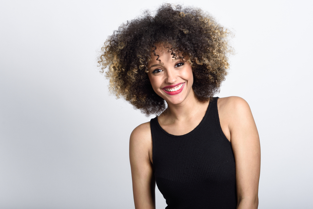 Young black woman with afro hairstyle smiling. Girl wearing black dress. Studio shot.. Young black woman with afro hairstyle smiling