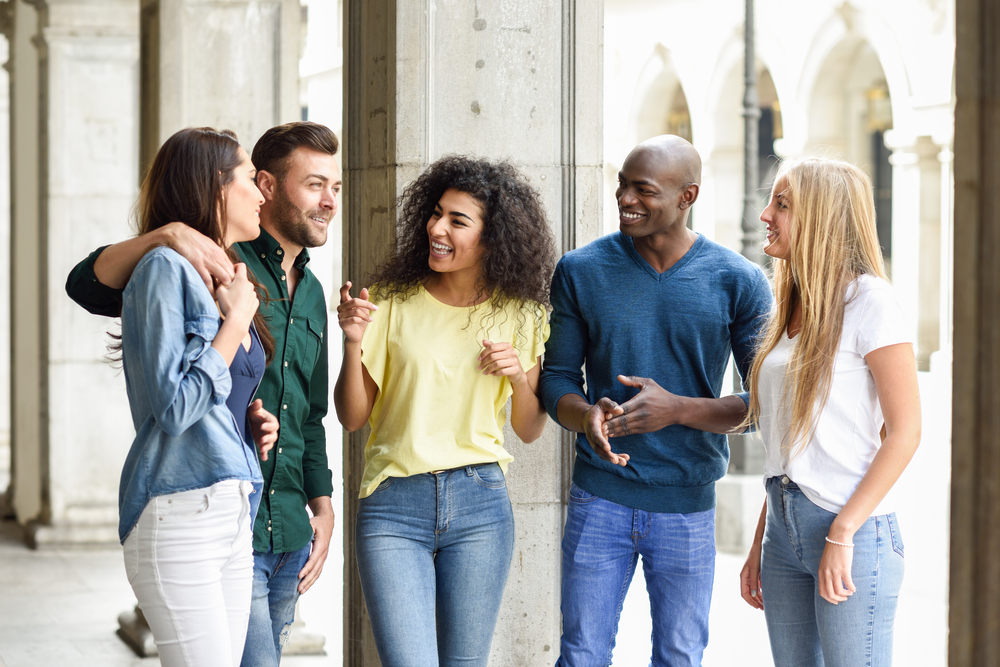 Multi-ethnic group of young people having fun together outdoors in urban background. group of beautiful women and men laughing together. Multi-ethnic group of friends having fun together in urban background