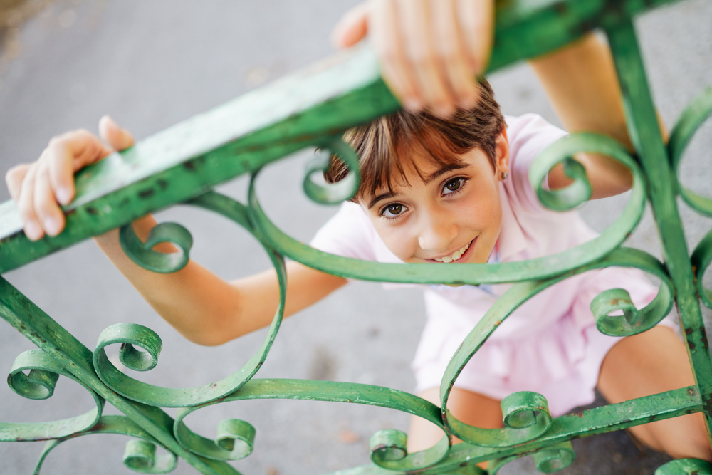 Little girl, with short hair, playing with a wrought iron fence. Little girl, eight years old, having fun in an urban park.