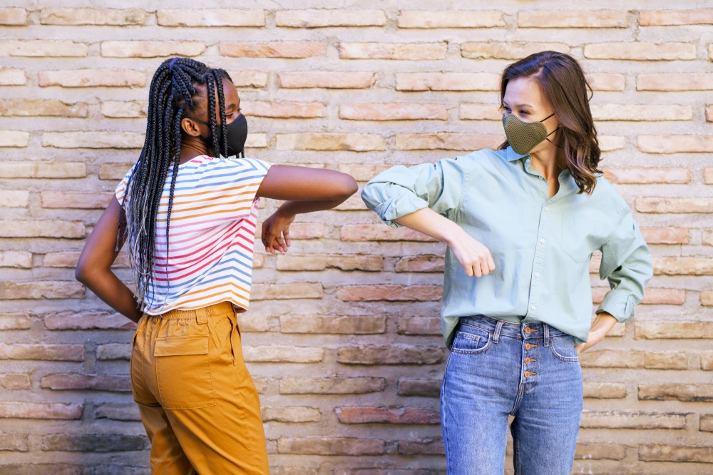 Multiethnic young women wearing masks greeting at each other with their elbows outdoors. Multiethnic young women wearing masks greeting at each other with their elbows