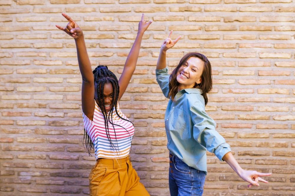 Two friends having fun together showing sign of the horns. Multiethnic women.. Two multiethnic women having fun together showing sign of the horns.
