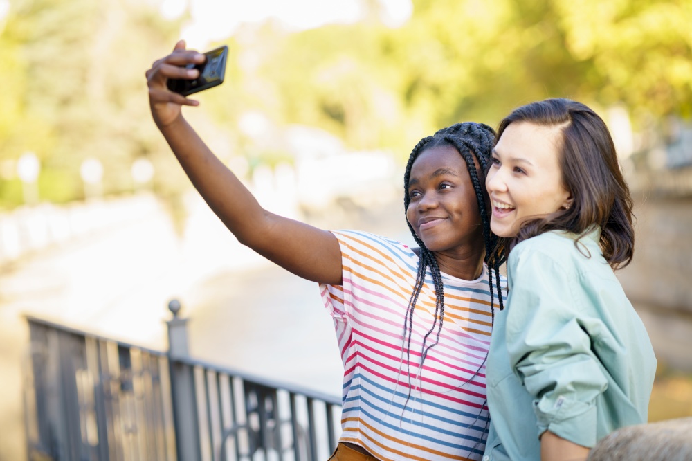Two multiethnic women making selfie with a smartphone outdoors.. Two multiethnic female friends making selfie outdoors.