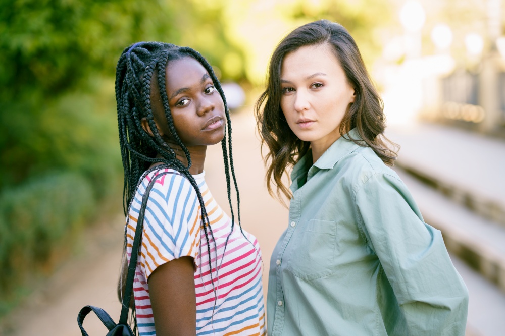 Two Multiethnic women looking at camera together on the street.. Two young friends looking at camera together on the street. Multiethnic women.