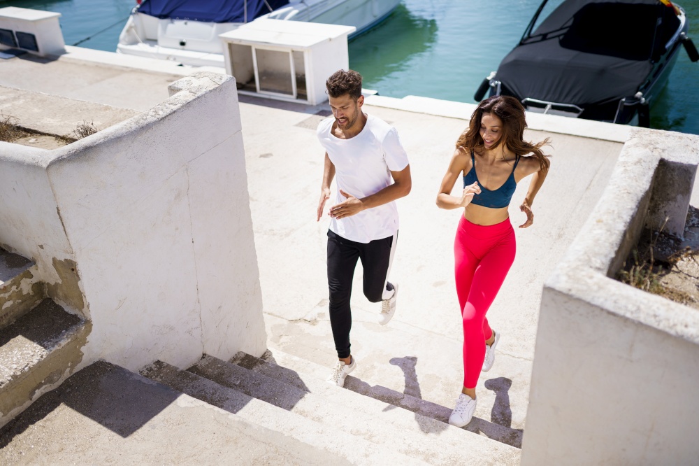 Athletic couple training hard by running up stairs together near the boats in a harbour. Athletic couple training hard by running up stairs together outdoors.