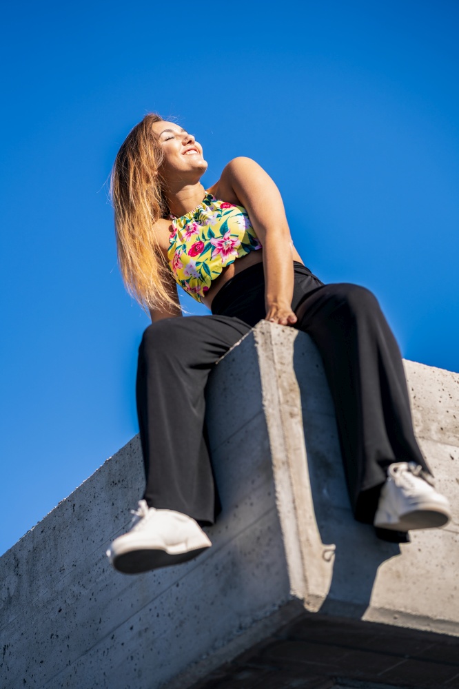 Funny young girl sitting on urban wall enjoying the sunlight. Funny young girl sitting on urban wall