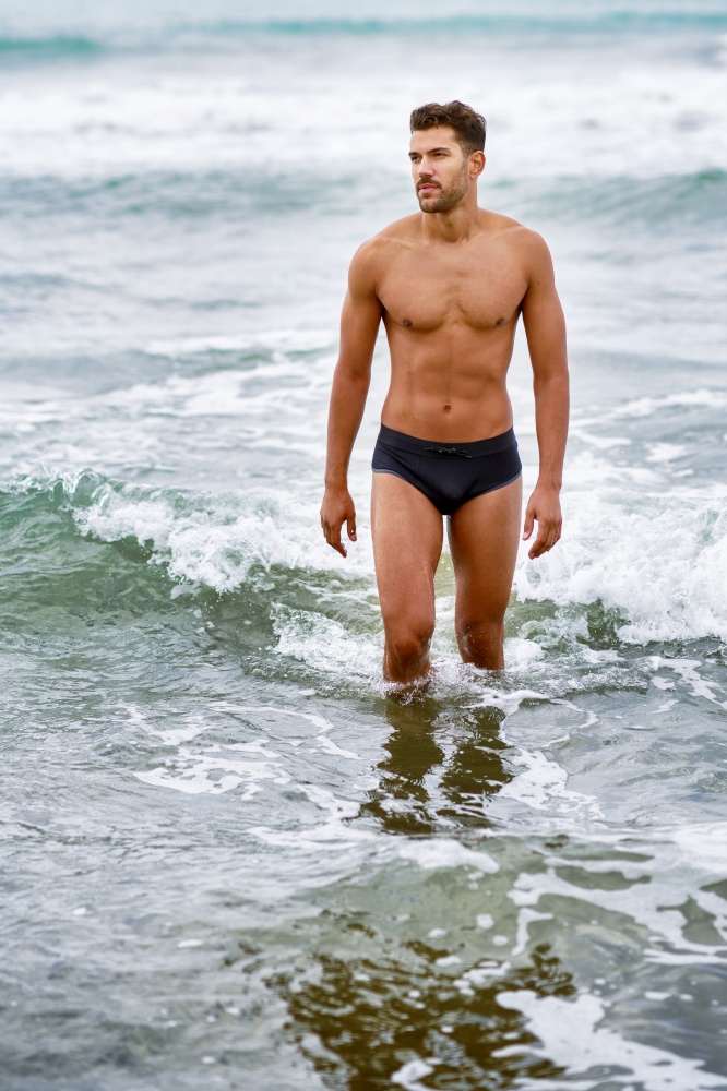 Handsome muscular man bathing on the beach wearing swimwear. Handsome muscular man bathing on the beach