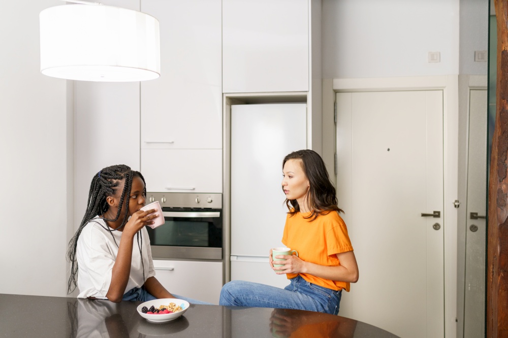 Two friends having a healthy snack while chatting at home. Multiethnic women.. Two friends having a healthy snack while chatting at home