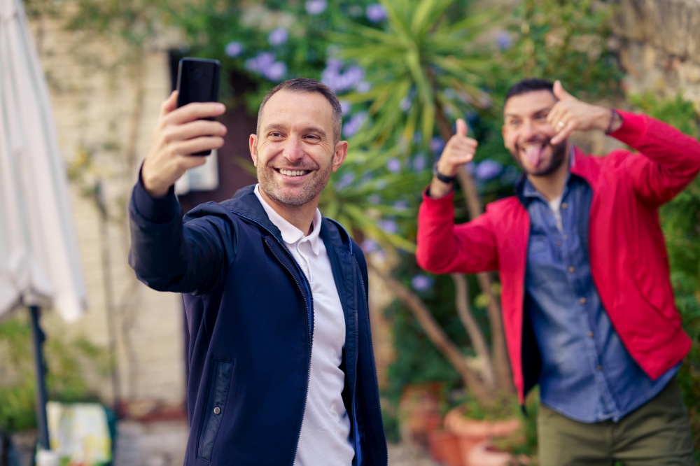 Gay couple making a fun selfie with their smartphone on the street. Lifestyle concept.. Gay couple making a fun selfie with their smartphone outdoor