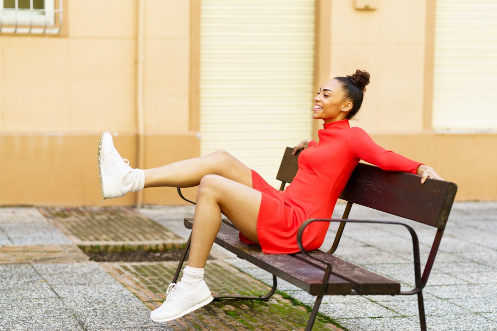 Happy mixed woman, waving her legs in joy, sitting on a bench in the street.. Happy mixed woman, moving her legs in joy, sitting on a bench in the street.