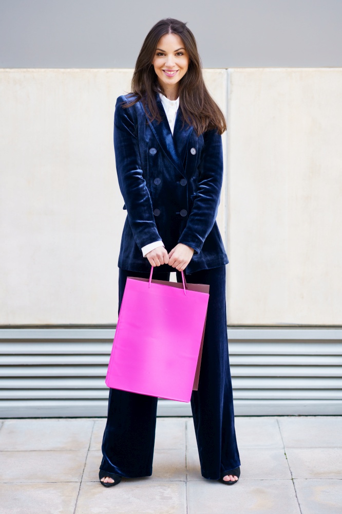 Young woman wearing blue suit carrying several shopping bags near a shopping mall. Lifestyle concept.. Young woman wearing blue suit carrying several shopping bags near a shopping mall.