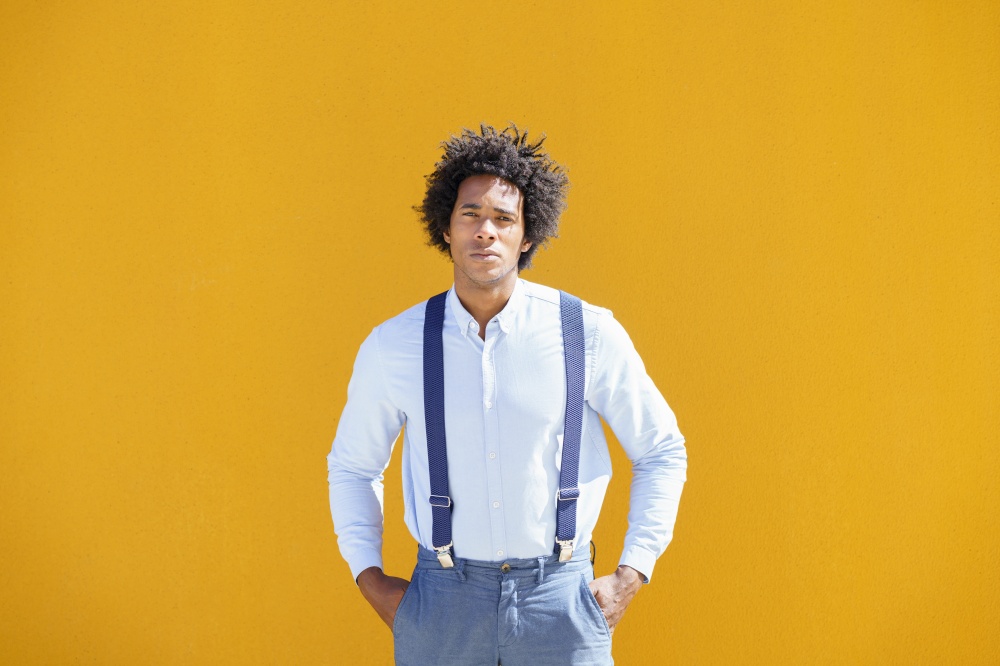 Attractive black man with afro hair on yellow urban background wearing shirt and suspenders.. Black man with afro hair on yellow urban background wearing shirt and suspenders.