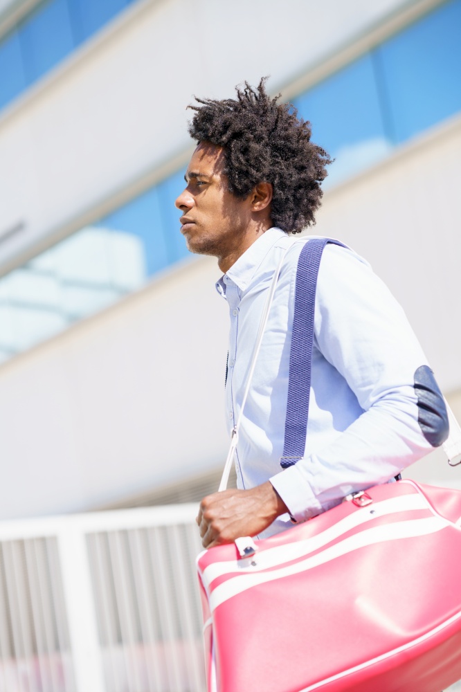 Black worker with afro hair walking near an office building with a sports bag.. Black worker walking near an office building with a sports bag.