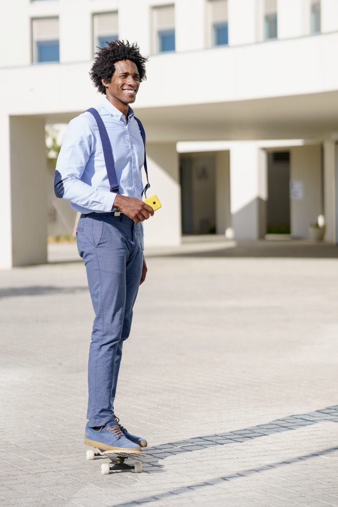 Black businessman on a skateboard holding a smartphone near an office building.. Black businessman on a skateboard holding a smartphone outdoors.