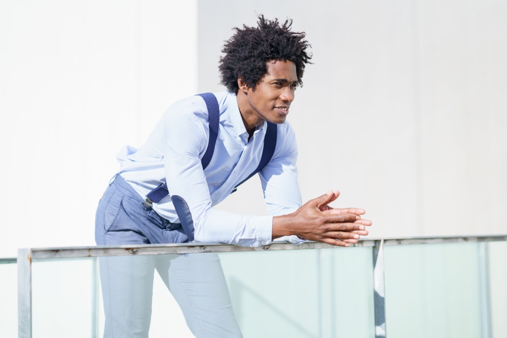 Attractive black businessman with afro hair, resting on a railing of his office building while looking at the horizon.. Attractive black businessman with afro hair, resting on a railing of his office building.