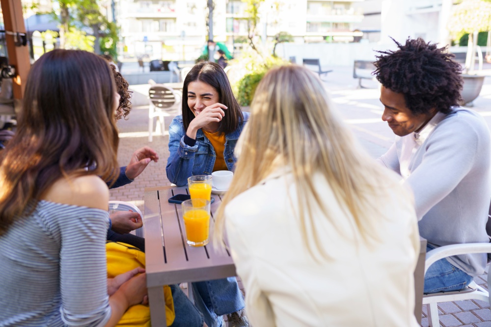 Multi-ethnic group of friends laughing and having a drink together in an outdoor bar.. Multi-ethnic group of friends having a drink together in an outdoor bar.