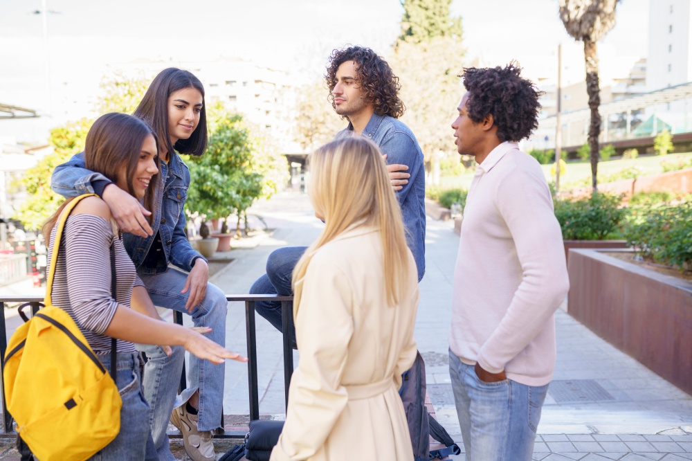 Multi-ethnic group of friends gathered in the street leaning on a railing. Young people having fun together.. Multi-ethnic group of friends gathered in the street leaning on a railing.