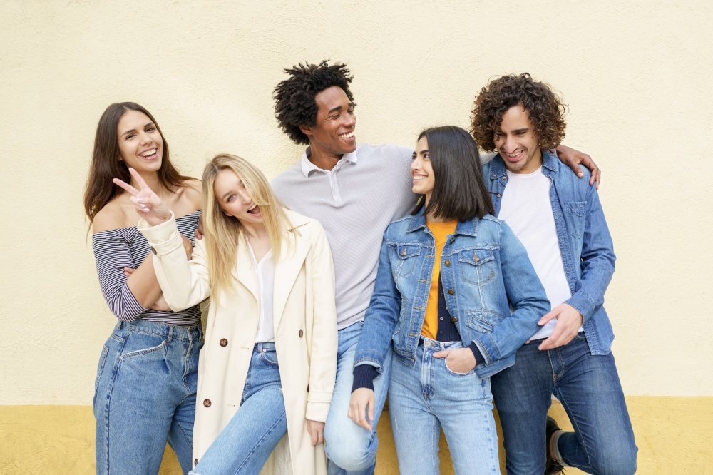 Multi-ethnic group of friends posing while having fun and laughing together against a yellow urban wall.. Multi-ethnic group of friends posing while having fun and laughing together
