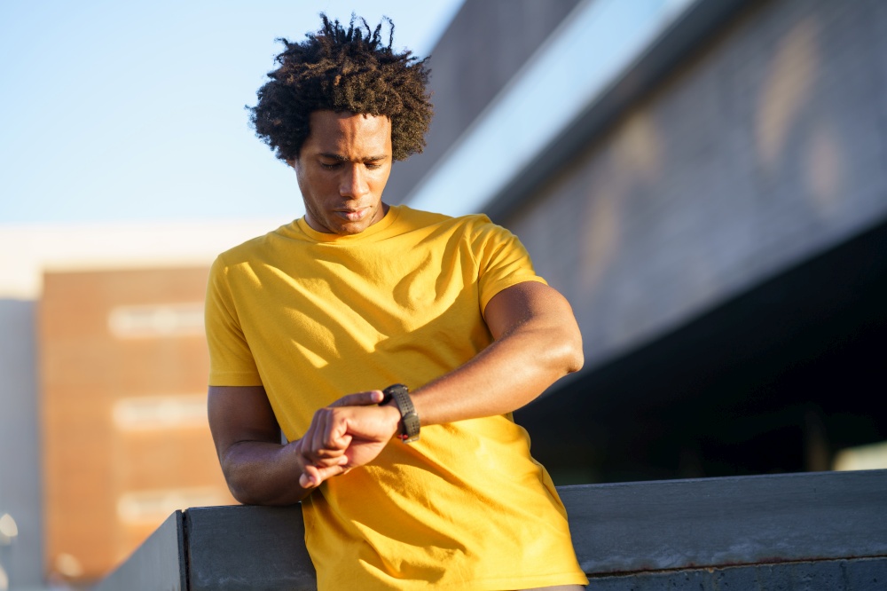 Black man with afro hair consulting his smartwatch to view his training data.. Black man consulting his smartwatch to view his training data.