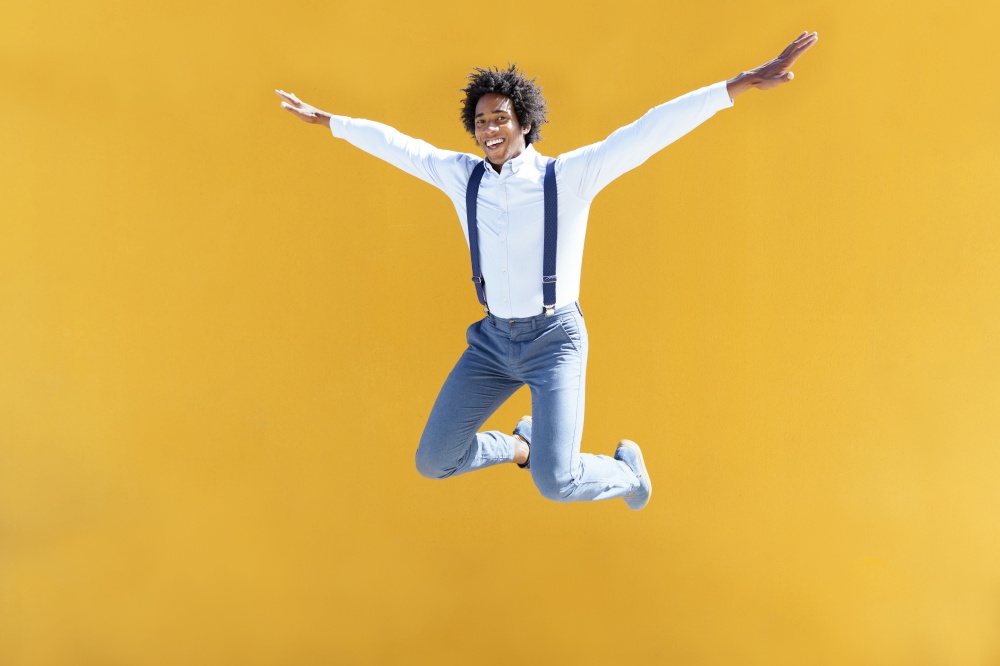 Black man with afro hair jumping on a yellow urban background. Guy wearing shirt and suspenders.. Black man with afro hair jumping on a yellow urban background