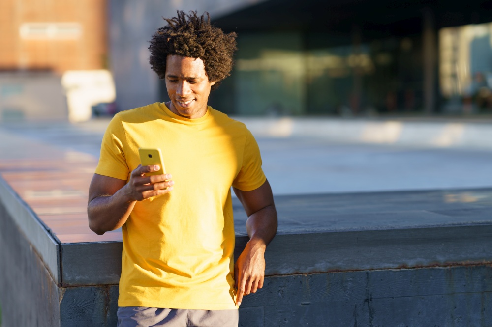 Black man with afro hair consulting his smartphone with some exercise app while resting from his workout.. Black man consulting his smartphone while resting from his workout.