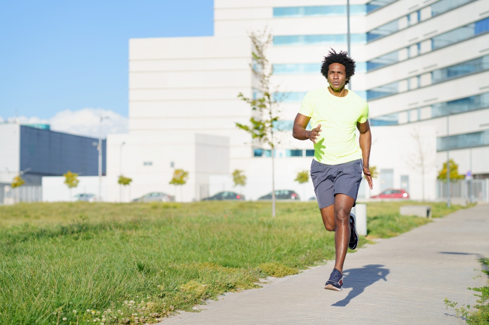 Black athletic man, afro hairstyle, running in an urban park. Young male exercising in urban background.. Black athletic man running in an urban park.