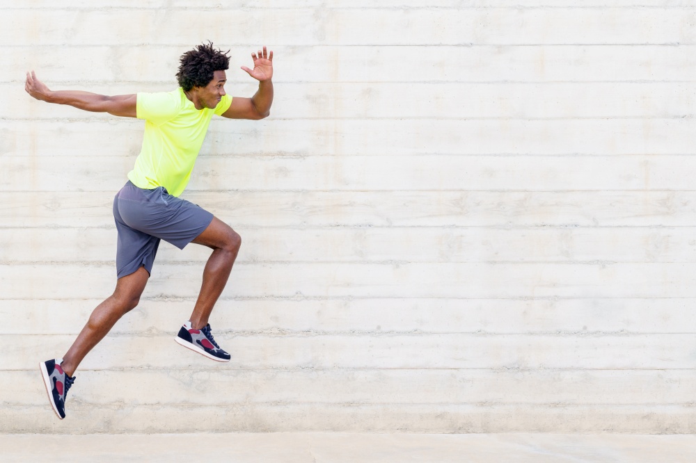 Black man training running jumps to strengthen his legs. Young male exercising in urban background.. Black man training running jumps to strengthen his legs.