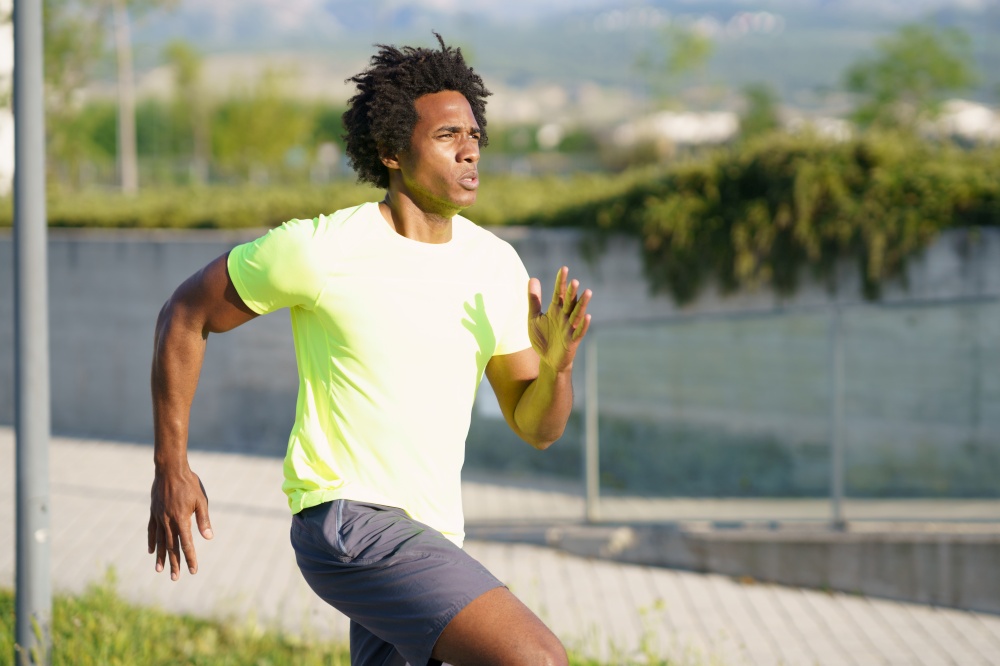 Black athletic man, afro hairstyle, running in an urban park. Young male exercising in urban background.. Black athletic man running in an urban park.