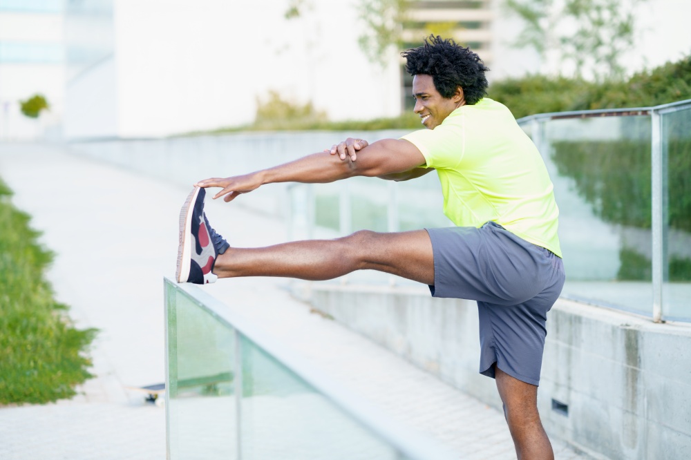 Black man with afro hair doing stretching after running outdoors. Young male exercising in urban background.. Black man with afro hair doing stretching after running outdoors.