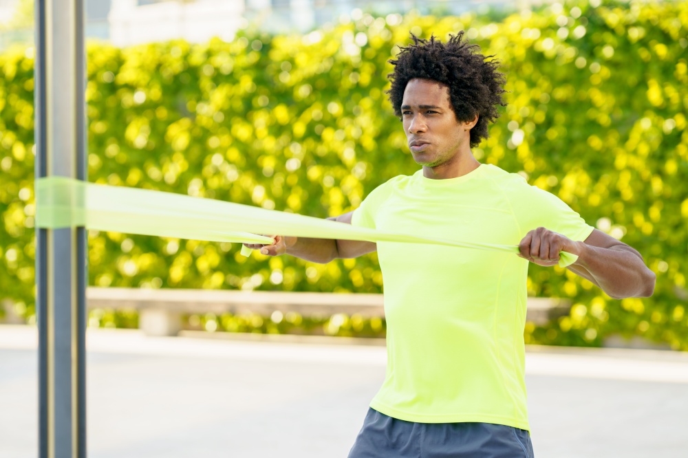 Black man working out with elastic band outdoors. Young male exercising in urban background.. Black man working out with elastic band outdoors