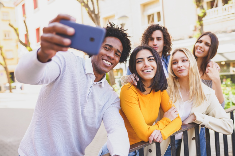 Multi-ethnic group of friends taking a selfie in the street with a smartphone. Young people having fun together.. Multi-ethnic group of friends taking a selfie in the street with a smartphone.