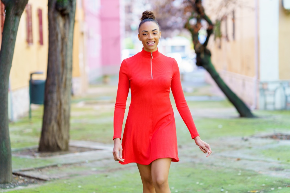 Smiling young mixed woman in red dress walking down the street. Smiling mixed woman in red dress walking down the street