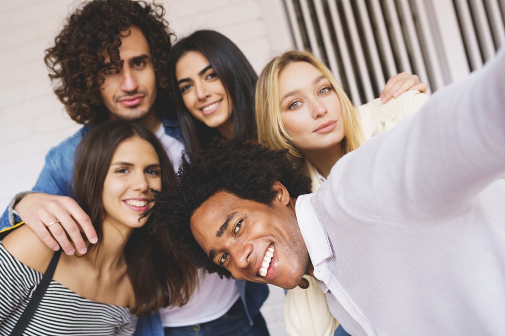 Multi-ethnic group of friends taking a selfie together while having fun in the street. Black man with afro hair in the foreground.. Multi-ethnic group of friends taking a selfie together while having fun outdoors.