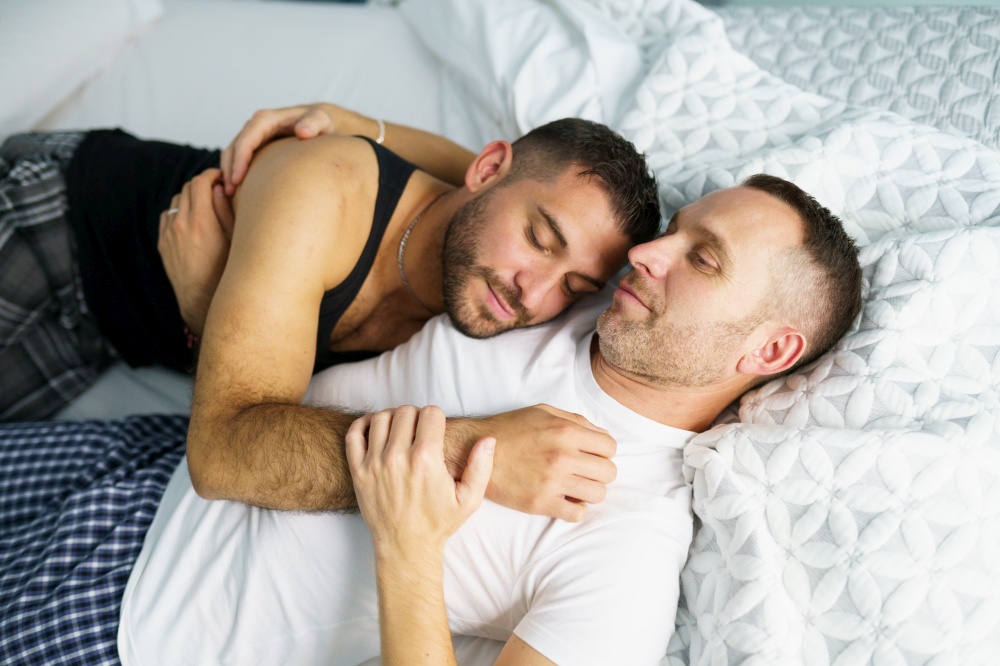 Gay couple in a romantic moment in bed. Homosexual lifestyle concept.. Gay couple sitting near the couch at home in a romantic moment