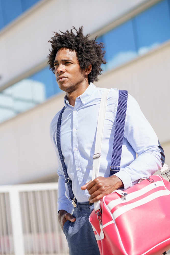 Black businessman with afro hair walking near an office building with a sports bag.. Black worker walking near an office building with a sports bag.