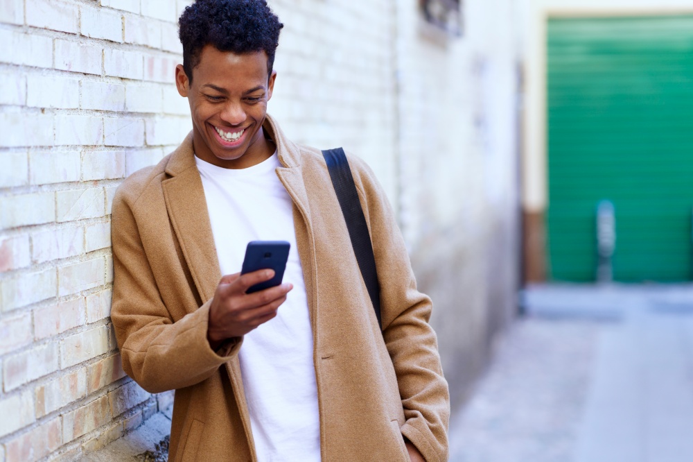 Young black man using his smartphone outdoors. Cuban guy smiling in urban background.. Young black man using his smartphone outdoors.