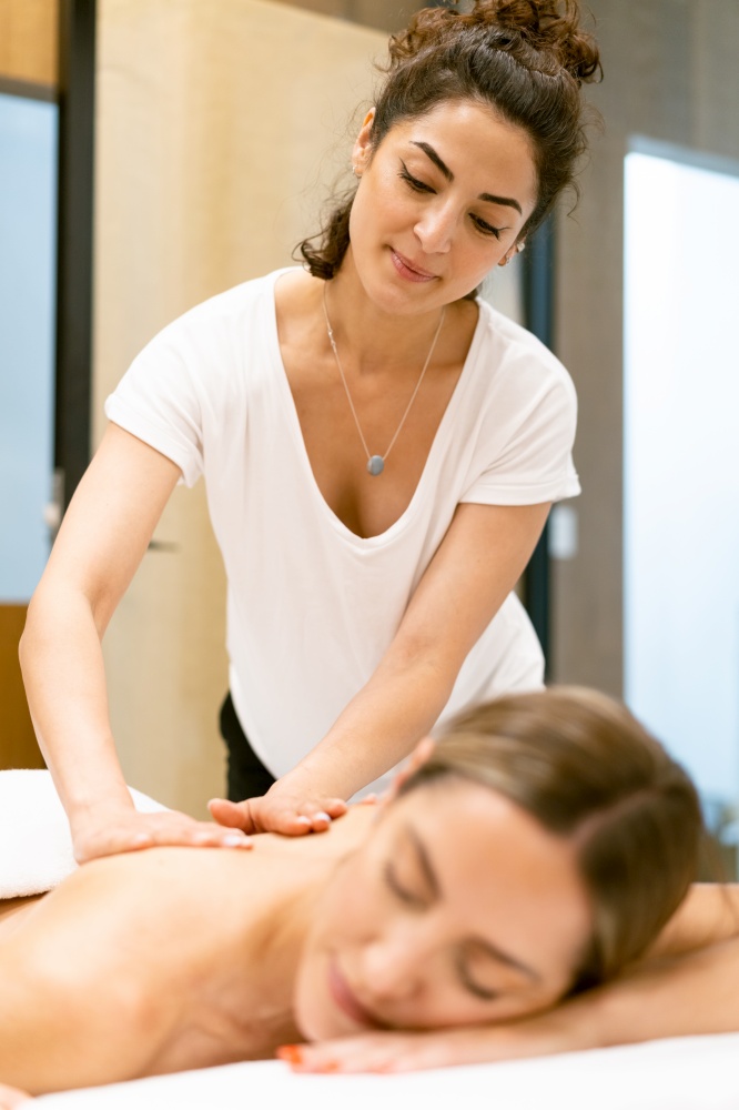 Female masseuse giving a back massage to a woman in a beauty parlour. Body care treatment in a beauty centre.. Female masseuse giving a back massage to a woman in a beauty parlour.