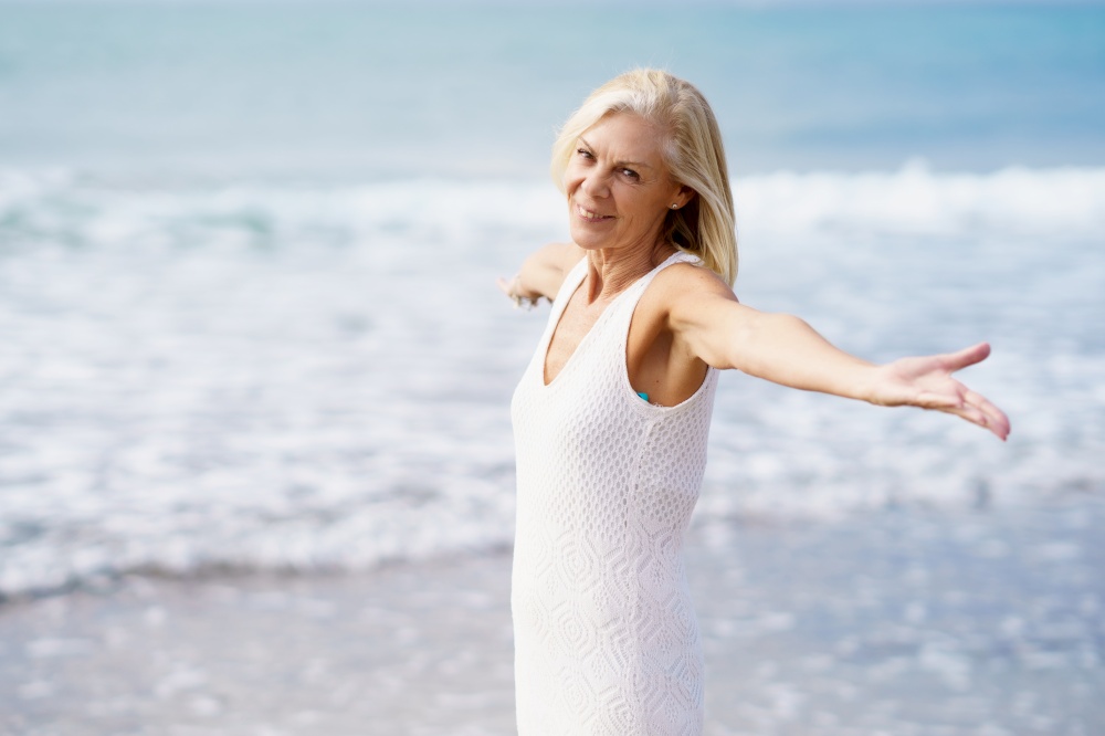 Mature female opening her arms on a tropical beach, spending her leisure time. Elderly woman enjoying her retirement at a seaside retreat.. Mature female opening her arms on the beach, spending her leisure time, enjoying her free time