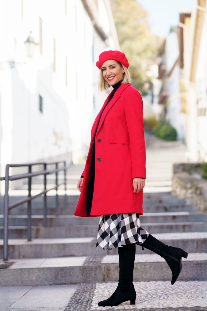Full body of trendy female in red beret looking at camera while strolling on stone staircase on street of city. Stylish woman walking on steps