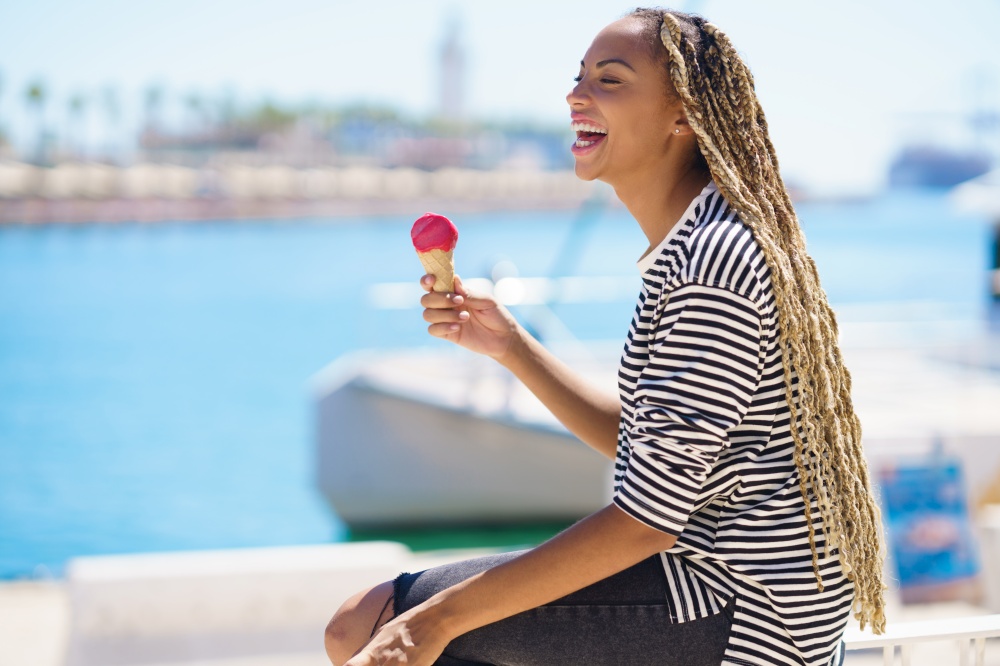 Beautiful young black woman eating a strawberry ice cream while enjoying the view of the seaport.. Black woman eating a strawberry ice cream while enjoying the view of the seaport.