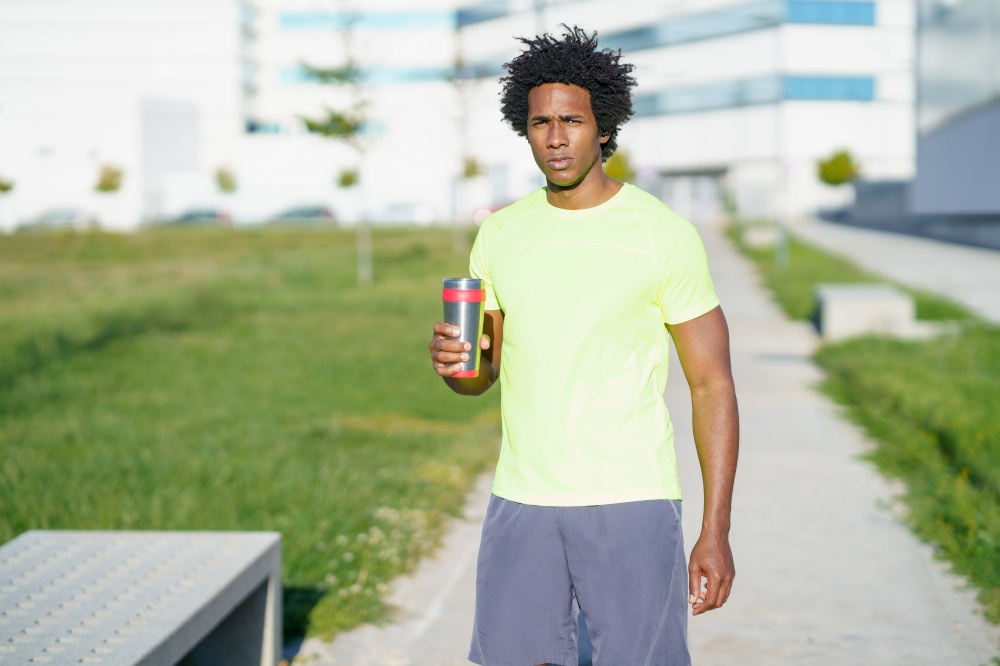 Tired African American male athlete standing with cup of water in street and having break during training in summer while looking at camera. Tired African American sportsman with water in city