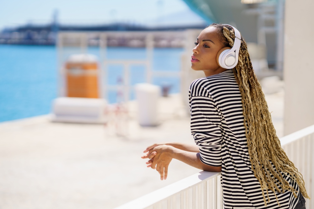 Beautiful young black woman listening to music while enjoying the view of the seaport.. Young black woman listening to music while enjoying the view of the seaport.