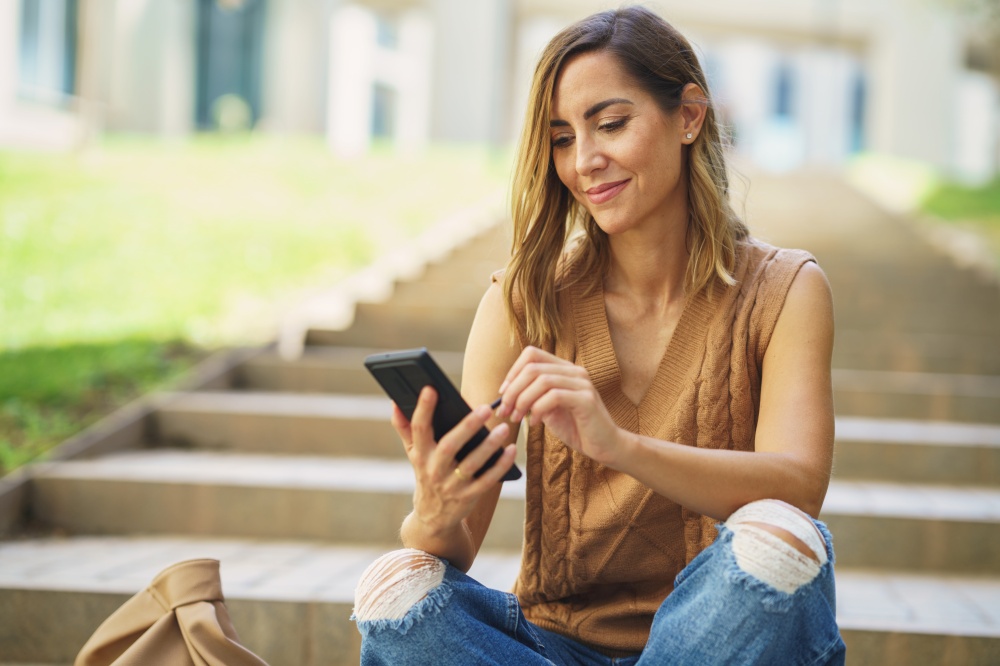 Middle aged using her smartphone with a pen or stylus, outdoor. Caucasian female wearing casual clothes.. Middle aged using her smartphone with a pen or stylus, outdoor.