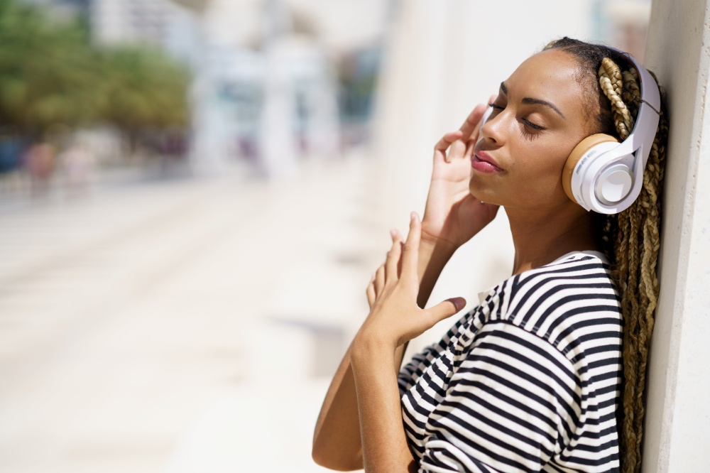 Beautiful young black female listening to music with wireless headphones outdoors.. Young black female listening to music with wireless headphones outdoors.