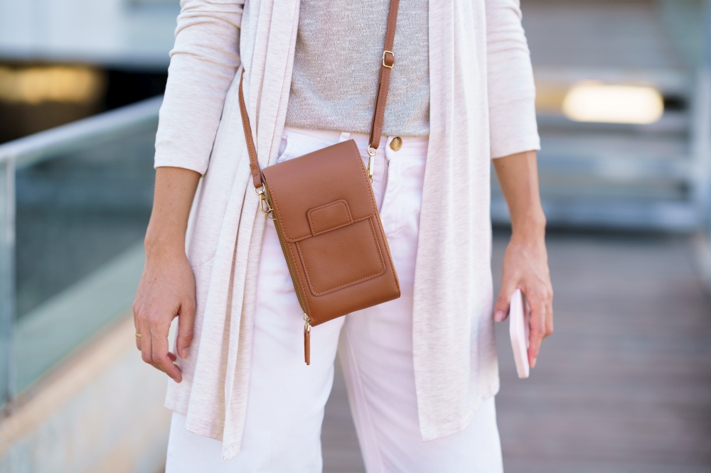 Unrecognisable woman standing near an office building carrying a handbag and a smartphone. Caucasian female in urban background.. Unrecognisable woman standing near an office building carrying a handbag and a smartphone.